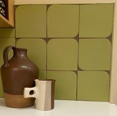 a brown and white vase sitting on top of a counter next to a green tiled wall