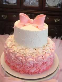 a three tiered cake with pink and white frosting on the top, decorated with bows