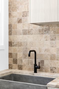 a kitchen sink with a black faucet in the middle and brown tiles on the back wall