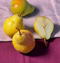 three pears and one apple on a purple cloth