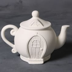 a white teapot with a door on the side and a cup in the middle