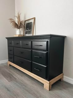 a black dresser sitting on top of a hard wood floor next to a white wall