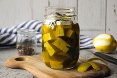 a jar filled with pickles sitting on top of a wooden cutting board next to lemons