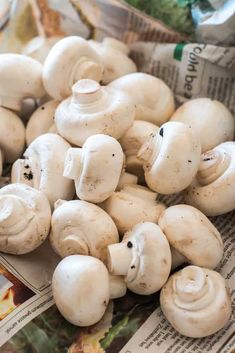 a pile of white mushrooms sitting on top of a newspaper