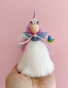 a hand holding a small doll with pink hair and white dress on it's finger