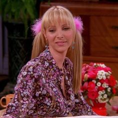 a woman with long blonde hair sitting at a table in front of flowers and a potted plant