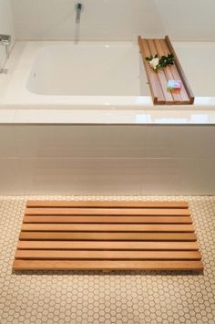 a bathroom with a bath tub and wooden slatted shower mat on the floor