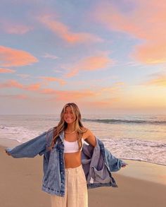 a woman standing on top of a beach next to the ocean holding onto a jacket