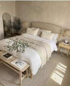 a large bed sitting next to a table with a plant on it in a bedroom