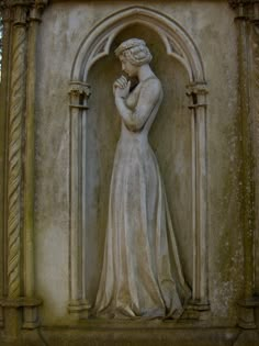 a statue of a woman holding her hands to her heart in front of a stone wall