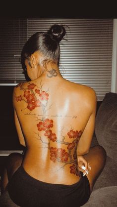 a woman with tattoos on her back sitting on a couch in front of a window