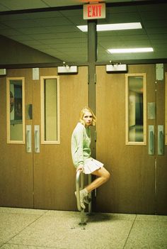 a woman leaning on a pole in front of an exit sign with her legs crossed