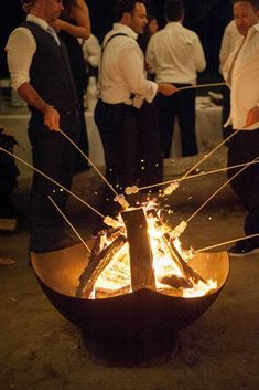 some people standing around a fire pit with sticks sticking out of it's sides