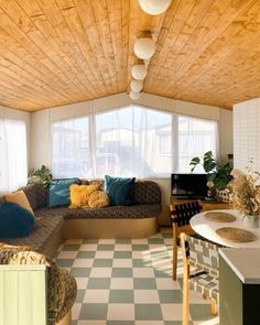 a living room with checkered flooring and wooden ceiling above the couch is a large window