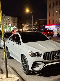 a white mercedes suv is parked on the side of the road at night in an urban setting