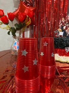 three red cups sitting on top of a table next to a vase filled with flowers