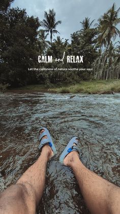 the feet of a man who is laying down in water with palm trees behind him