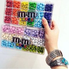 a person holding up a plastic container filled with candy beans and m & m's