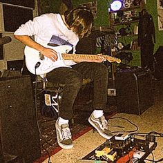 a young man sitting on top of a chair playing an electric guitar in a room