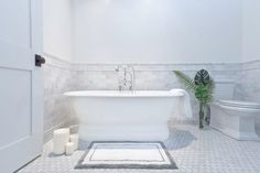 a white bathtub sitting next to a toilet and a plant in a room with tile flooring