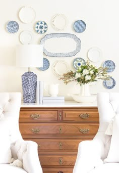 two white chairs sitting in front of a dresser with blue and white plates on it