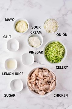 ingredients to make chicken salad laid out on a white marble counter top with the names in different bowls