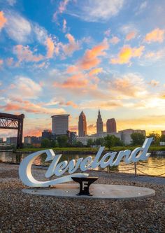 the cleveland sign is sitting on top of a bench in front of a river and cityscape