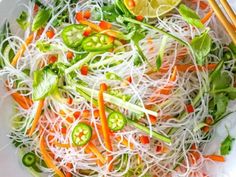 a white bowl filled with vegetables and veggies next to chopsticks on a table