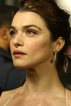 a close up of a woman wearing earrings and looking off into the distance with other people in the background