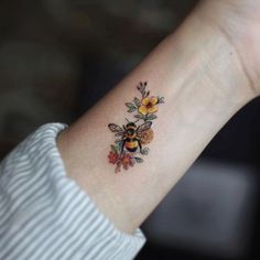 a woman's arm with a tattoo on it that has flowers and a bee