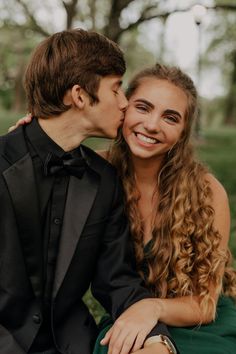 a young man and woman sitting next to each other on a bench in the grass