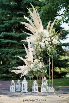 an arrangement of white flowers and candles are on display in front of some pine trees