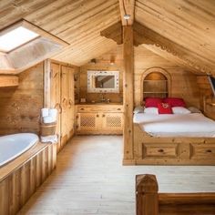 a bedroom with wooden walls and flooring has a large bed in the corner, along with a white bathtub