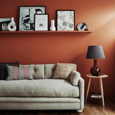 a living room with an orange wall and some pictures on the shelf above it,