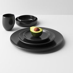 an avocado sitting on top of a black plate next to two cups and saucers