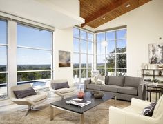 a living room filled with lots of furniture and large windows overlooking the trees in the distance