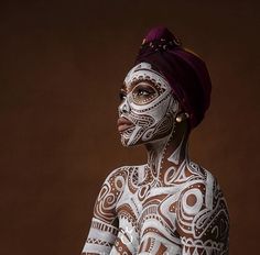 a woman with white paint on her face and body is standing in front of a brown background