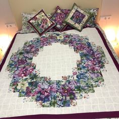 a quilted bed with purple and white flowers on the bedspread, along with two lamps