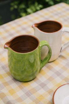 two green and brown coffee mugs sitting on top of a checkered table cloth