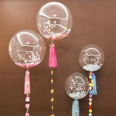 three clear balloons with tassels hanging from them on a brown wall next to stars and confetti