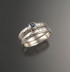 two silver rings with blue sapphire stones on them sitting on a black surface in front of a gray background