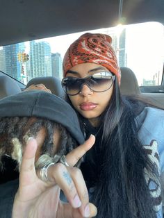 a woman in sunglasses and a hat holding up her peace sign while sitting in the back seat of a car