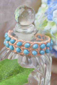 a close up of a perfume bottle with beads on it and flowers in the background