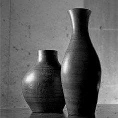 two black vases sitting on top of a table next to each other in front of a wall