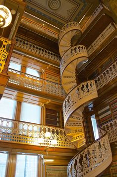 a spiral staircase in the middle of a room with many bookshelves and windows