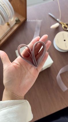 a person holding a heart shaped object in their hand with scissors and other items on the table behind them