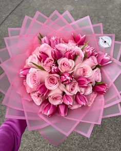 a bouquet of pink flowers sitting on top of a purple piece of paper in someone's hand