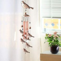 a bird wind chime hanging from the side of a window next to a potted plant