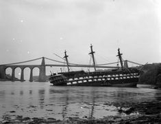 an old ship sitting in the water near a bridge