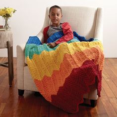 a little boy sitting in a chair with a blanket on top of him and smiling at the camera